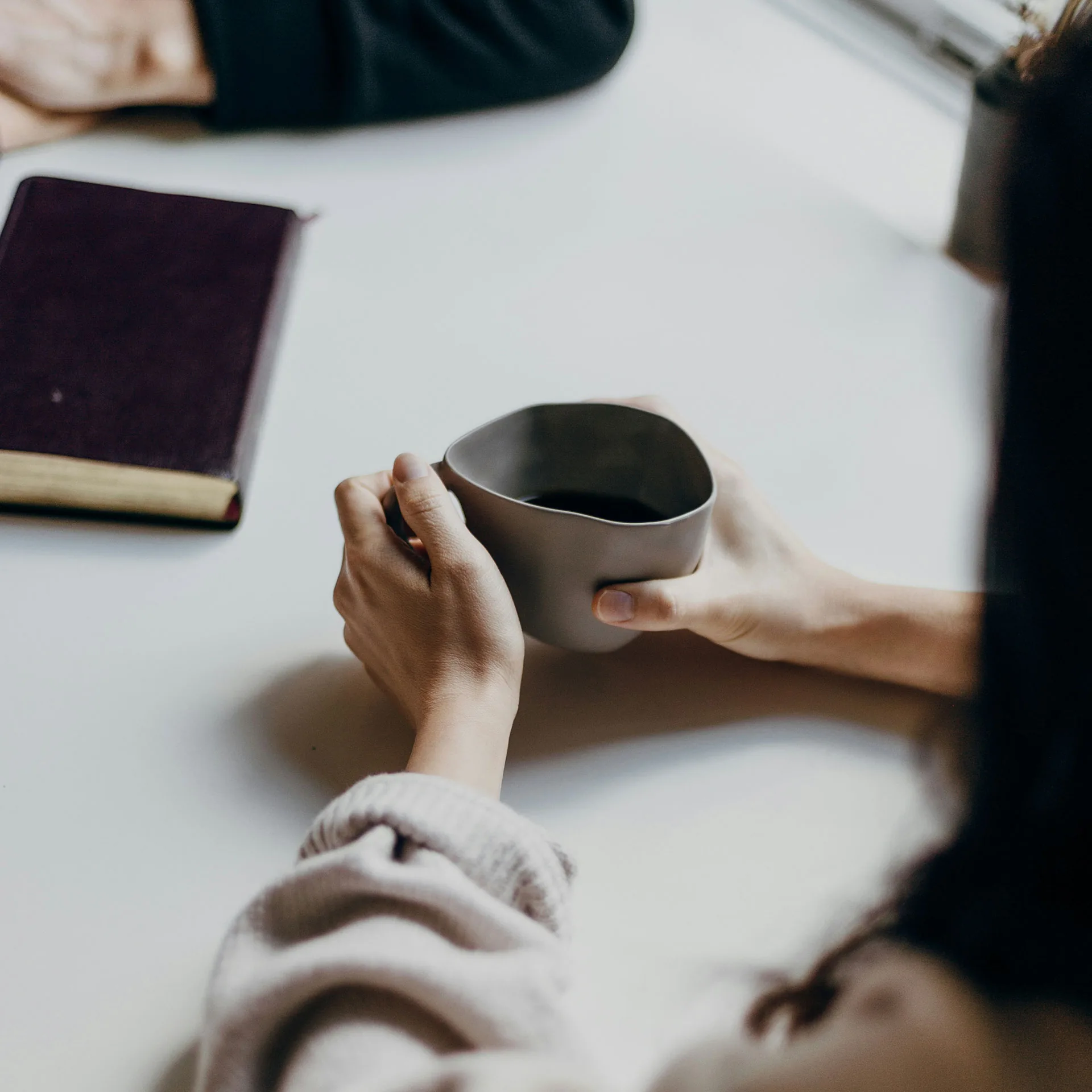 Närbild på händer med kaffekopp med anteckningsbok i bakgrunden